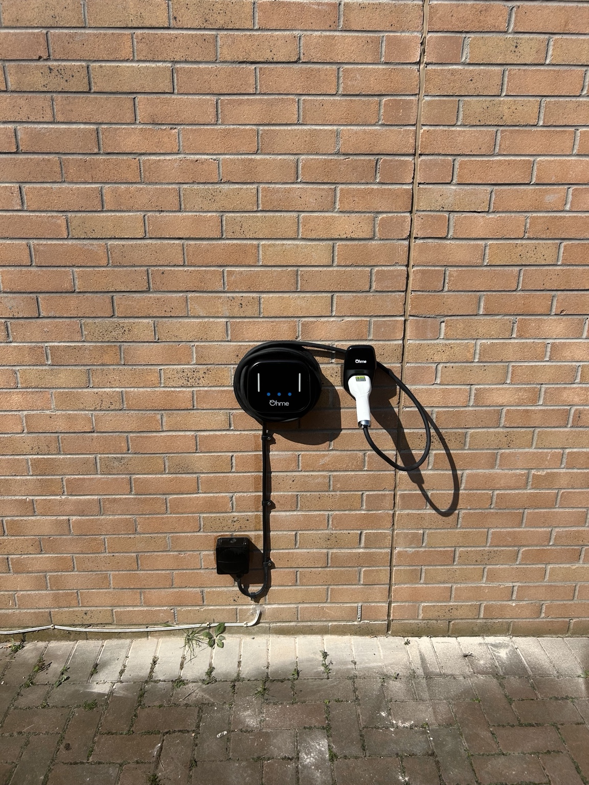 Ohme EV charger mounted on a garage wall with neatly clipped cabling
