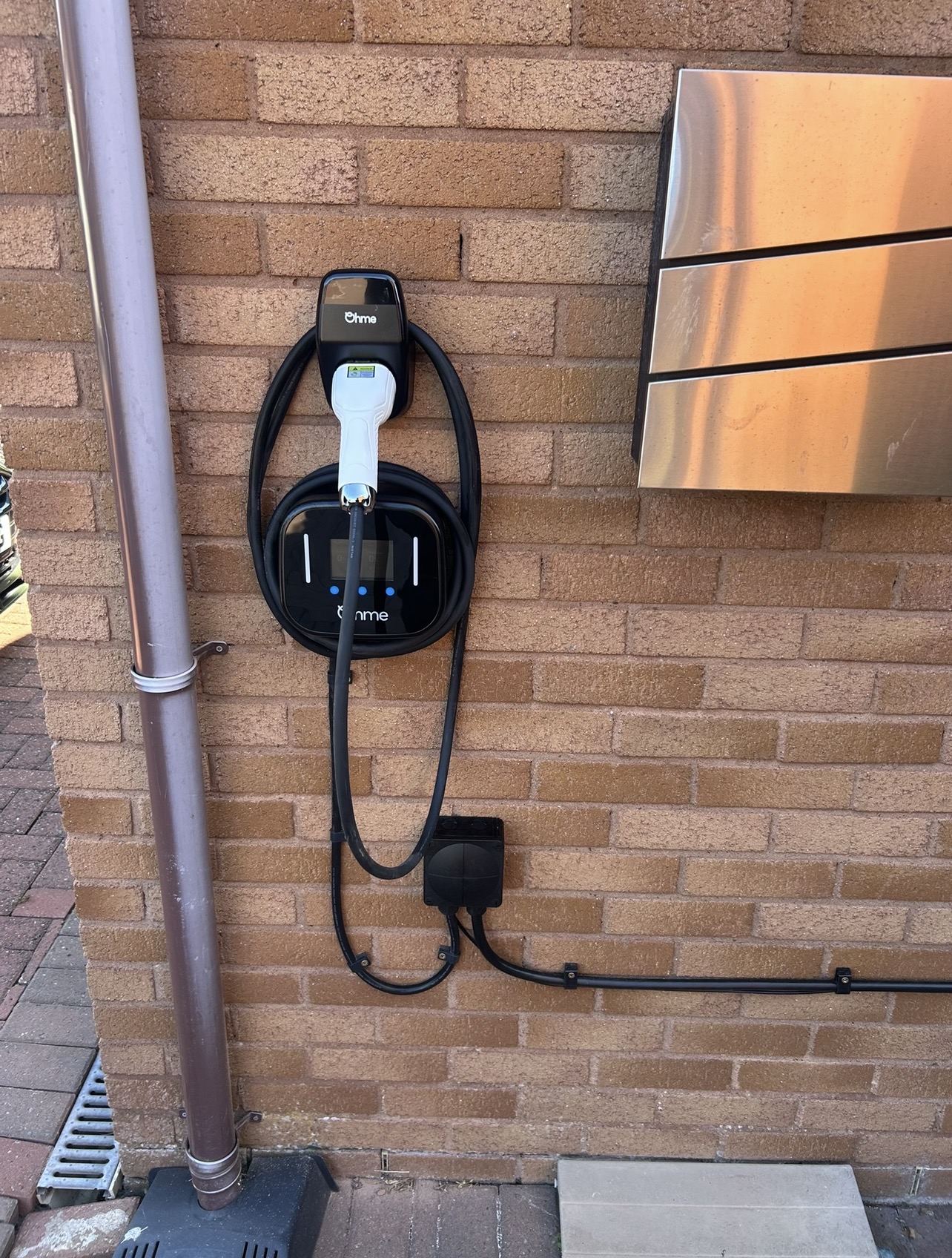 Ohme home EV charger with tethered cable installed on a brick wall